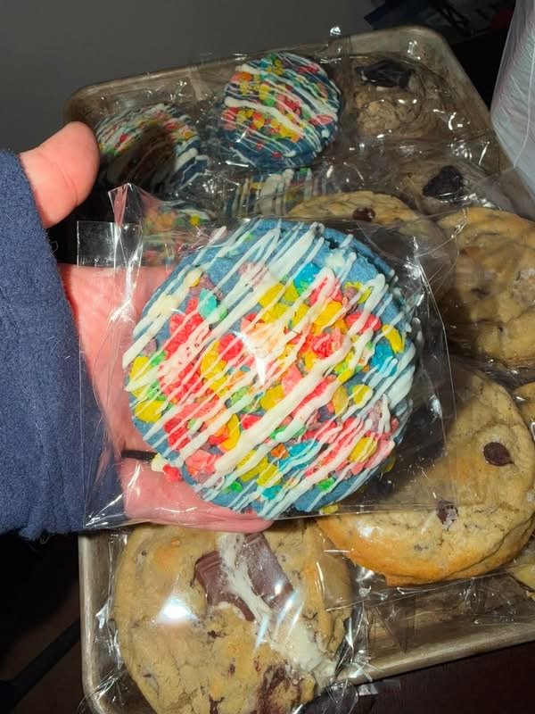 Fruity Pebbles-covered cookie held up in front of a cookie tray